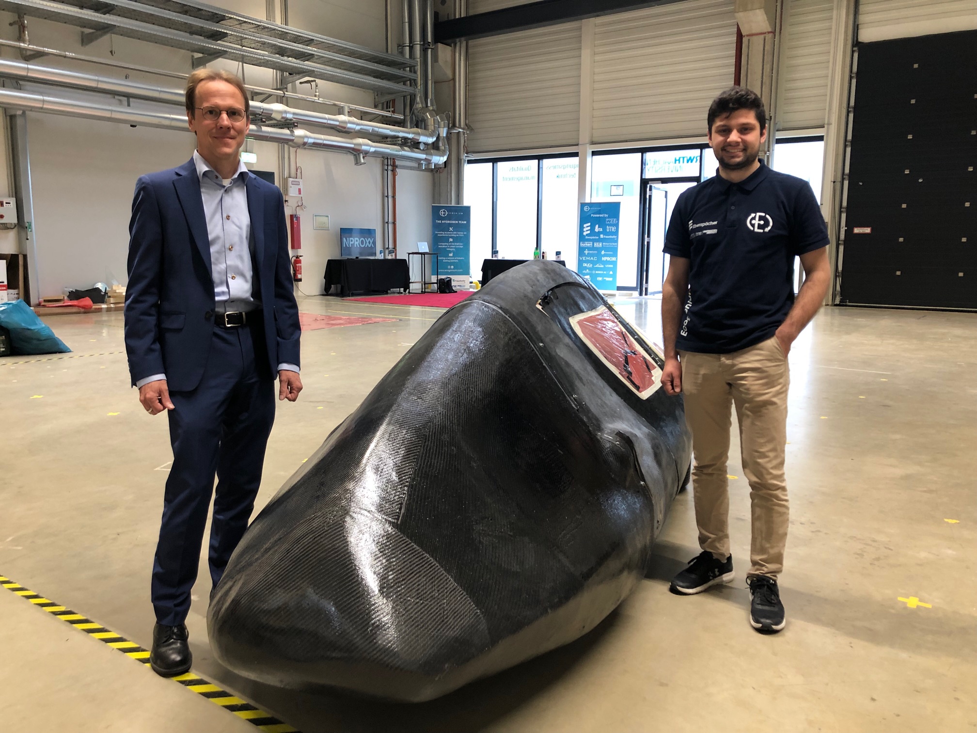 Klaus Peter Kopper standing with a member of the Ecogenium team with the Fuel Cell Electric Vehicle
